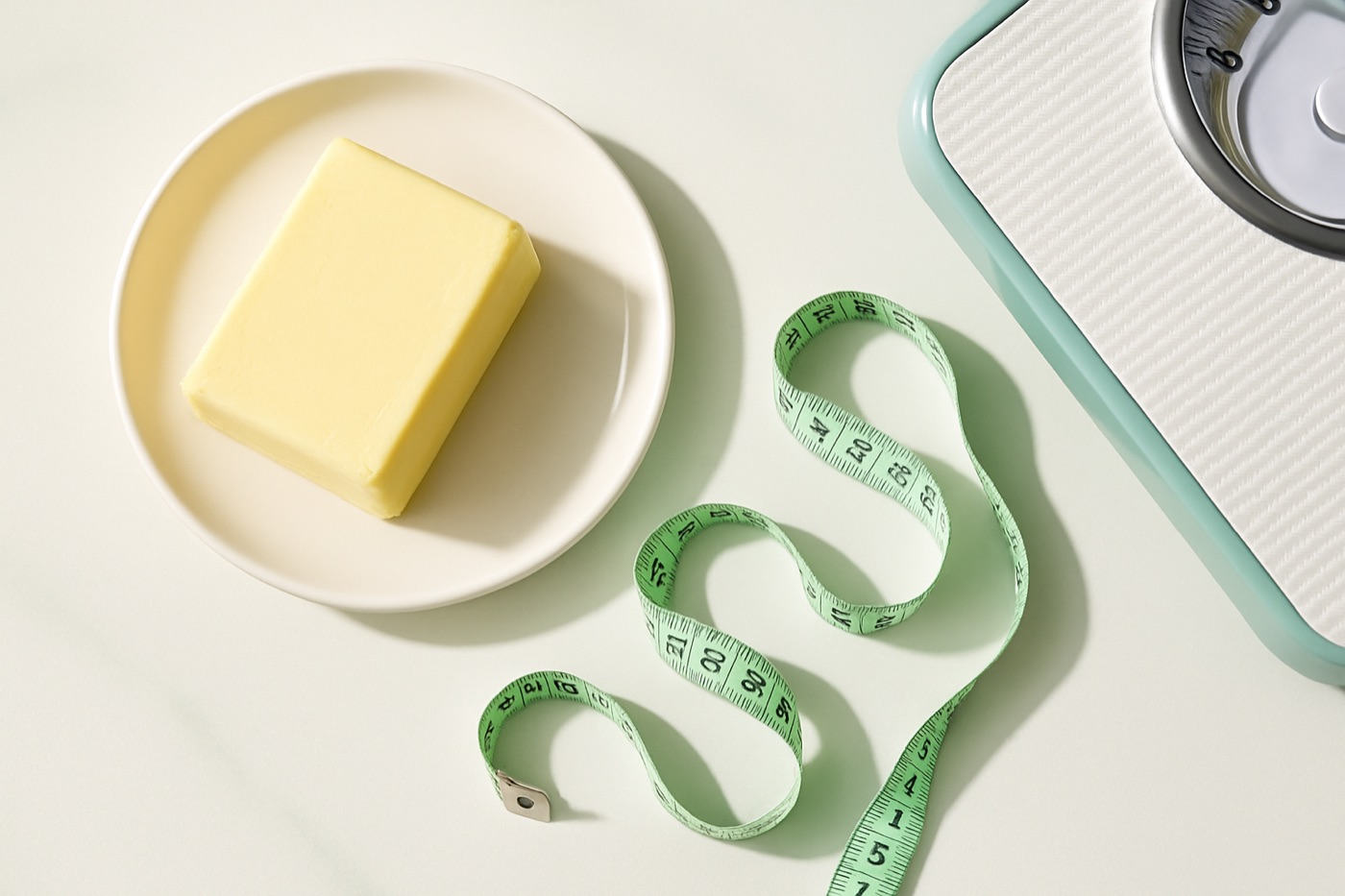 A one-pound block of butter beside a measuring tape and a bathroom scale, photographed from above